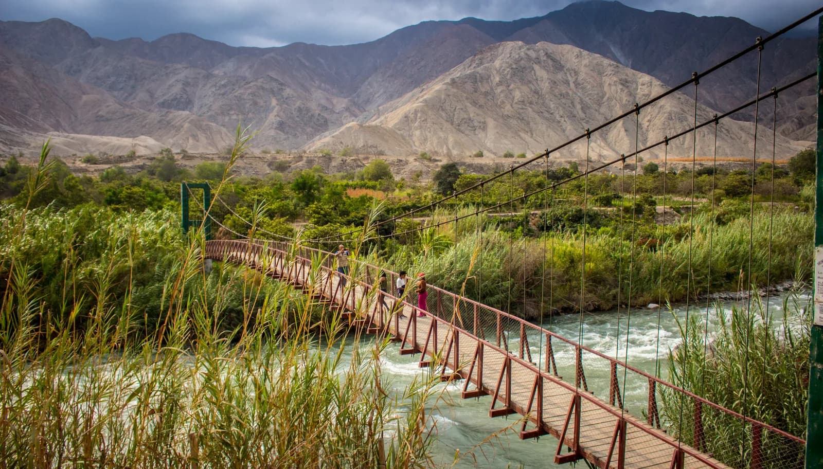 Wooden hanging bridge stretching across the Río Cañete near Lunahuaná with dry Andean foothills behind
