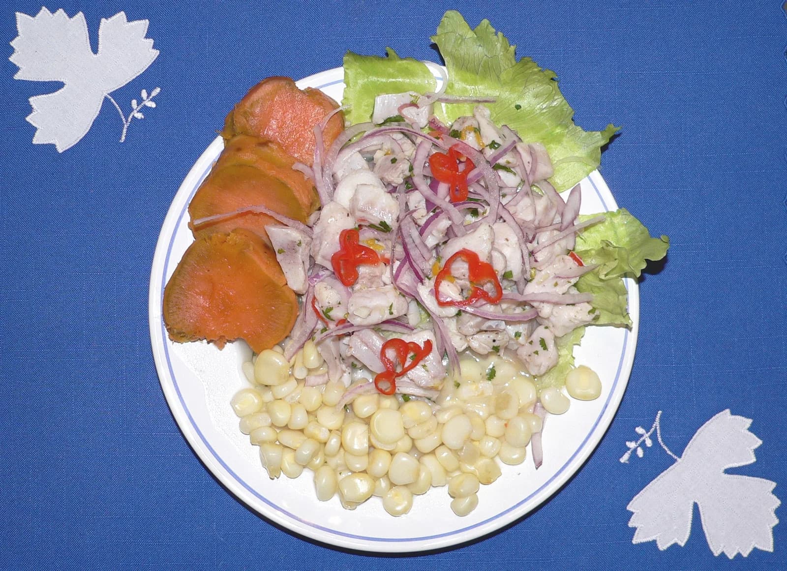 A plate of Peruvian ceviche with red onion, sweet potato and corn, served with a glass of white wine